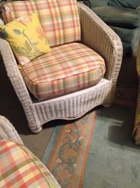 One of two white wicker chairs with colorful plaid fabric; large pastel colored rug