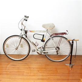 Vintage Peugeot 501 Bicycle and a leyne pump: A vintage Peugeot 501 bicycle with tire pump. This twelve speed bicycle is white and has a red book rack over the rear tire. The Peugeot 501 was produced in the 1980s.