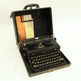 Vintage Royal Portable Typewriter: A vintage Royal portable typewriter. This heavy black metal typewriter features a paper roller with the feed marked “Royal”, black typing keys with white lettering, margin release, carriage return and ribbon. The original paperwork is included.