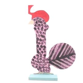 Marvin Finn Folk Art Quail Sculpture: A hand-crafted wood quail sculpture by Marvin Finn (1913 – 2007). This folk art piece is made of a carved, flat board mounted on a wood base. It depicts a stylized quail with a red plume and purple, black, and white body and tail feathers. The base is painted light blue. The piece is signed “2000 Finn” on the underside. Marvin Finn was born in Alabama and starting producing unique folk art in 1972.