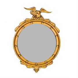 Federal Style Round Wall Mirror: A Federal style round wall mirror. This gold tone round wooden wall mirror features an eagle figure on the top with leaf garland accents to top and bottom. The mirror is unmarked.
