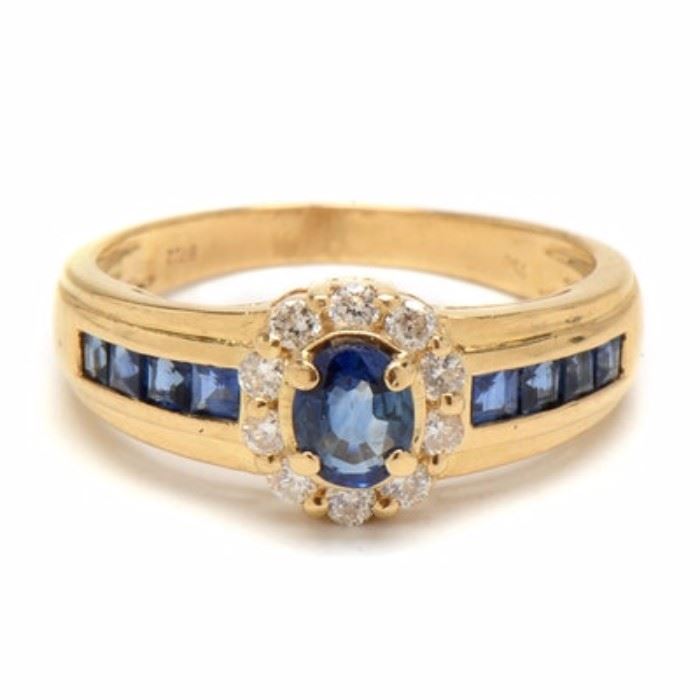 18K Yellow Gold Natural Blue Sapphire Diamond Ring: An 18K yellow gold ring featuring a natural blue sapphire surrounded by a wreath of diamonds with additional natural blue sapphires to the shoulders.