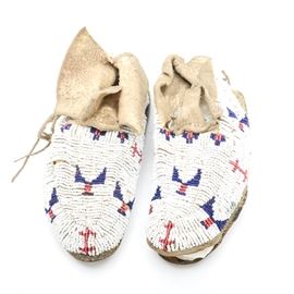 Antique Cheyenne Native American Beaded Moccasins: A pair of antique Native American Cheyenne child sized moccasins, circa 1900. With elaborate and painstaking detail, the moccasins are beaded in white with red and cobalt designs on deer hide with stiff soles and sinew stitching. Traditionally the soles of moccasins were made of the same leather as the teepee, as the smoke rendered the material waterproof.
