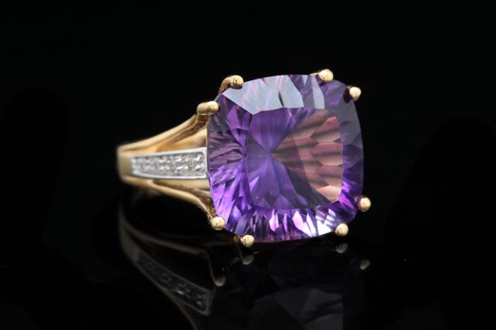 18K Gold, Amethyst, and Diamond Ring: An 18K two-tone gold, amethyst, and diamond ring featuring a cushion cut amethyst set with 18K yellow gold prongs. The shanks feature an accent 18K white gold bar embellished with diamonds.
