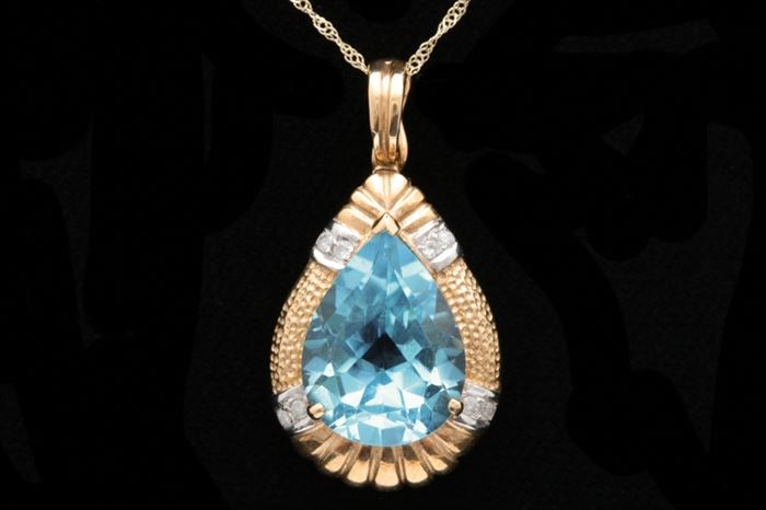 14K Yellow Gold, Blue Topaz and Diamond Pendant with Chain: A 14K two-tone yellow gold, blue topaz and diamond pendant with chain. The pendant features a prong set, pear-shaped blue topaz gemstone accented with eight round brilliant diamonds set with 14K white prongs within two bars of white gold. The yellow gold frame is textured with small round dents. The bail is also a pearl enhancer. Included is an 18" 14K yellow gold cable chain with a spring ring clasp.