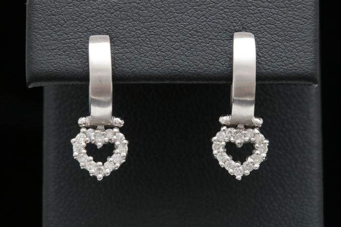 14K White Gold and Diamond Heart Earrings: A pair of 14K white gold and diamond heart earrings. The huggy hoops suspend hearts lined with a total of twenty-four round brilliant diamonds.