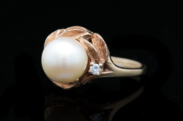 14K Gold, Pearl and Diamond Ring: A 14K gold, pearl and diamond ring featuring a pearl accented with a single round brilliant diamond and circled with etched 14K yellow gold leaves.