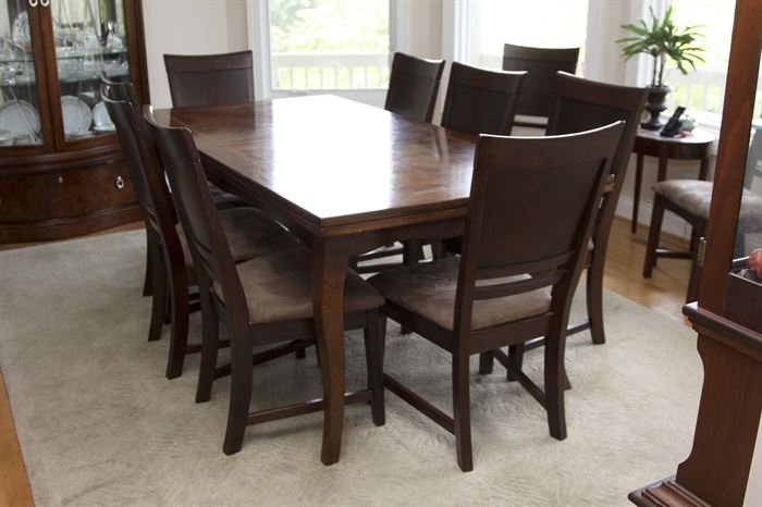 Broyhill Dining Table and Ten Chairs: A Broyhill dining table and ten chairs. This rectangular shaped table features a mahogany finish with inlaid top and end extensions resting on four cabriole style legs. Also included are ten mahogany finished side chairs with solid head and back rests, beige brushed suede style upholstered seats resting on four legs with stretchers to the sides.