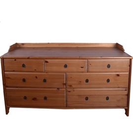 Pine Dresser: A pine dresser. The dresser features a rectangular top with carved back rail, oval brass hardware, three single drawers at the top, and four double drawers below. This sale features a matching tall dresser and pair of nightstands: 17CIN381-002 and 17CIN381-013.