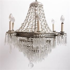 Austrian Crystal Chandelier: An Austrian crystal chandelier. Featured here is a large ceiling hanging chandelier with a wide silver tone filigree metal band around the center section. Attached to the center band are six candlestick style light sockets with hanging crystal prisms around their bases. The interior of the light has an additional three light sockets. The bottom portion of the light features tapered rows of metal rings adorned with hanging crystals. A spherical crystal ball dangles from the bottom. The top portion has a crystal chain canopy leading up to a scalloped crystal cap. Paperwork included with the chandelier indicates that it was originally hung in the Ogden Theater. No maker’s marks.