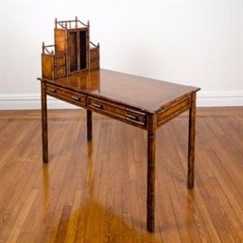 Regency Style Faux Bamboo Desk: A Regency style faux bamboo desk. This piece has a honey hued finish. It features organizational cubbies and a center cabinet with wire lattice door fronts to the left side of the top. To the front of the desk are two half-width drawers with brass-toned pulls. To the right side, below the top is a pull-out work surface. The desk rises on four legs resembling gathered bamboo.