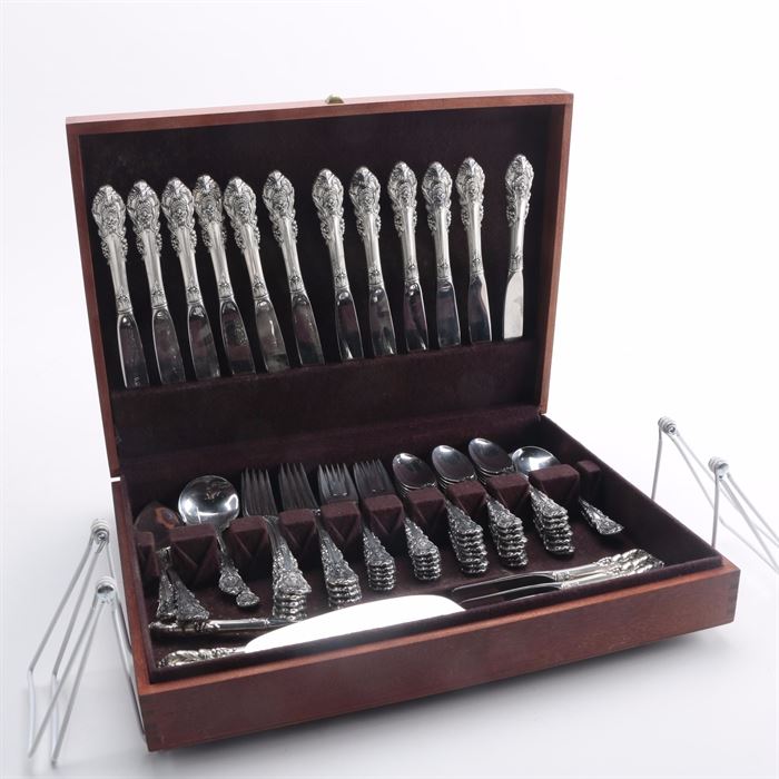 Wallace "Sir Christopher" Sterling Flatware in Chest: A group of sterling flatware in the Sir Christopher pattern by Wallace, presented in a wooden chest. There are eighty-one pieces in total including twenty-four spoons, twelve salad forks, twelve dinner forks, and additional dining utensils including a ladle. Also included are eleven dinner knives, eight butter spreaders, a cake knife, a carving fork and a pie server, all with stainless blades and hollow handles. These items are presented in a wooden chest. The total approximate weight is 66.025 ozt excluding items with stainless elements.