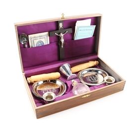 Priest Sick Call Box: A priest sick call box. Included is one crucifix, one silver plated spoon, one absorbent cotton pack, one sick call instruction sheet, one small handkerchief, two silver tone trays, one small chalice, one glass holy water bottle, and two candles. All pieces are stored in a wooden box that is marked with a cross along the exterior.