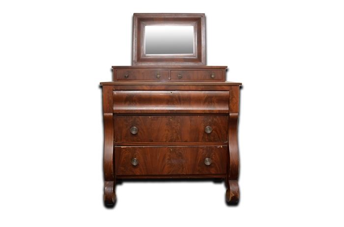 Vintage Empire Style Dresser: A vintage Empire style dresser. This dresser features a rectangular top with a removable vanity piece and mirror over a set of drawers. The piece rises on serpentine stiles terminating in scroll feet. The dresser has a flame mahogany veneer.