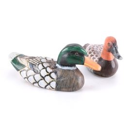 Duck Figurines: A pair of duck figurines. This pair of wooden decoys features hand painted features and includes a duck with green head and a duck with orange head. with detailed brown and white feathers.