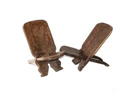 Pair of African Birthing Chairs: A pair of African birthing chairs. This hand rendered pair has been constructed from solid mahogany, with carved designs of a crocodile on one, and a warrior mask on the other. Each chair consists of two pieces of wood that simply pull-apart for storing. The use of these chairs dates from antiquity and are still in use today.