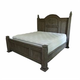 Spanish Revival Style Bed With Mattress: A Spanish Revival style bed with mattress. This piece is oak and includes the headboard, footboard, rails, and mattress. The headboard has an arched center, with raised panels and a carved shield and leaf motif, and square stiles with turned finials. The footboard features three horizontal recessed panels, between square stiles. The bed stands on square block feet.