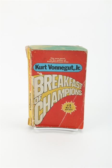 Circa 1974 Paperback Edition of "Breakfast of Champions" by Kurt Vonnegut Jr: A vintage edition of Breakfast of Champions by Kurt Vonnegut Jr. This paperback edition was printed by Dell Publishing Co., Inc. in March of 1974. The first page is marked with a blue tone stamp labeled “American Book & News Agency, Athens.”