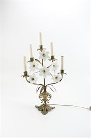 White Flower Candelabra: A white flower candelabra. The iight is a brass metal with a tree design that features decorative white flowers throughout. Other features include five branches with metal flower shaped pans and white sleeves, a leaf shaped vase cap and decoratively scrolled stem that stands on a grass shaped brass base with metal feet.