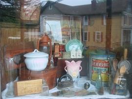 An assortment of items available at sale.  Old tins and boxes with advertising, irons, rolling pins, egg beaters, bottles, vases, chamber pot, railroad lantern, art prints, postcards, etc.