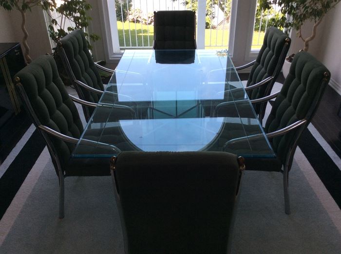 Chrome and glass dining table with six moss green button-tufted chairs.