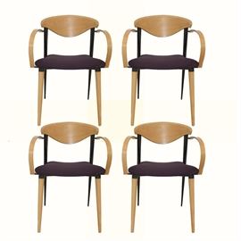 Modern Style Maple Armchairs: A set of four modern-style maple armchairs. Each of these chairs features a curved crest and short back, supported by tapered black stiles which continue into legs. Their arms are curved, leading to the plum-upholstered seats. They rest on tapered legs.