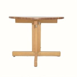 Oak Dinette Table: An oak dinette table. This piece is oak, with the circular top formed from multiple blocks of wood in various finish shades. The top rests on a pedestal base of four planks forming an X, with a plank foot extending out from the bottom of each, with metal tab feet.