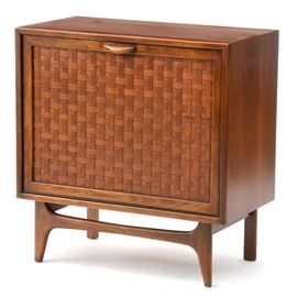 Walnut LP Record Cabinet: A Walnut LP-record cabinet, having a fall-front door with a basket woven walnut panel, opening to a divided bin. The case rests on a framed base. Circa 1970.