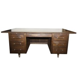 Alma Desk Company Mid-Century Desk: A vintage Alma kneehole office desk. The desk features a faux wood laminate top with wood veneer sides and front and square wood legs. The desk features a center locking drawer and three drawers to right and two drawers including a file drawer to the left. The desk has satin finished nickel hardware.