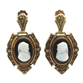14K Yellow Gold Onyx Cameo Earrings: A pair of 14K yellow gold onyx cameo earrings. Each earring features a central cameo depicting the profile of a woman. The cameo is surrounded by an ornate, abstract frame dangling from a hinged top.