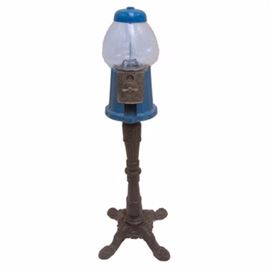 Blue Gumball Machine on Wrought Iron Stand: A blue gumball machine on a wrought iron stand. This gumball machine features a clear glass sphere encased by blue metal with a silver tone coin mechanism and dispenser to its front. The gumball machine is presented on a turned and tapered wrought iron stand resting on four claw feet.