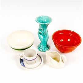 American Pottery Including Lenox: An assortment of American pottery including Lenox. Included in this assortment are an orange mixing bowl marked “Bauer 06”, a white and green mixing bowl marked “Oven Proof USA”, and a swan-shaped dish marked “Lenox, Made in USA”. Also included are a blue hand-shaped vase marked “USA”, and a white teacup and saucer with blue stripes and an “Antoine Restaurant” design marked “Syracuse China, 93-D, 92-K, USA”.