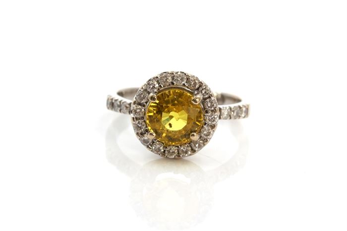 18K White Gold 1.95 CTS Yellow Sapphire and Diamond Ring: A round faceted yellow sapphire is prong set to a halo of diamonds that travel down a quarter of the way to the white gold shank.