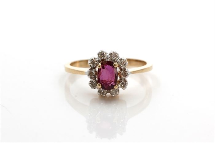 10K Yellow Gold Ruby and Diamond Ring: A faceted oval cut ruby is prong set to a halo of round cut diamonds on a reverse tapered yellow gold shank.