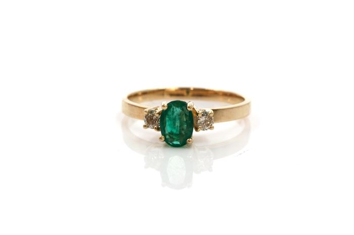 14K Yellow Gold Emerald and Diamond Ring: An oval faceted emerald is basket prong set to the center of a traditional yellow gold shank and accented by round cut diamonds on the shoulders.
