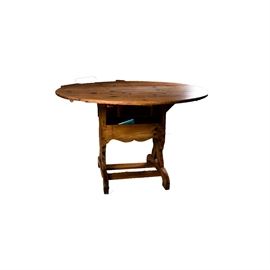 Vintage Round Pine Table: A vintage round pine table. This table features a round top over a middle support with a serpentine apron and storage space. the table rises on a pair of legs with trestle base.