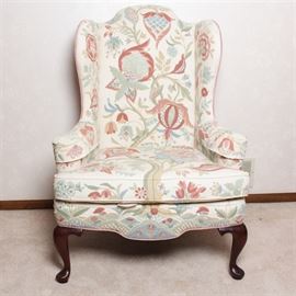 Vintage Woodmark Original Crewel Embroidered Wingback Chair: A vintage Woodmark Originals crewel embroidered wingback chair. This Queen Anne style chair has front cabriole legs with bun feet. It has a cream toned background with pastel light blue, sage green, pink and peach embroidered flowers throughout. Armrest covers are included. The back and sides are covered in a soft peach material. It has a maker’s tag under the seat cushion and Copyright Mary Webb Wood 1976.