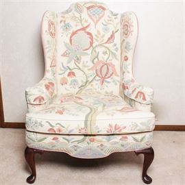 Vintage Woodmark Original Crewel Embroidered Wingback Chair: A vintage Woodmark Originals crewel embroidered wingback chair. This Queen Anne style chair has front cabriole legs with bun feet. It has a cream toned background with pastel light blue, sage green, pink and peach embroidered flowers throughout. Armrest covers are included. The back and sides are covered in a soft peach material. It has a maker’s tag under the seat cushion and Copyright Mary Webb Wood 1976.