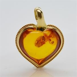 18K Yellow Gold Amber Puff Heart Pendant: An 18K yellow gold amber puff heart pendant. The heart-shaped amber is mounted in a rope trimmed hand formed bezel and with a generous top bale.
