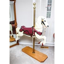 Cast Metal Carousel Horse: A cast metal carousel horse. This cast metal piece features a white painted body with burgundy tack and golden accents. It is attached to a brass pole and rests on an oak base. Base of pole is marked “1/4 Made in U.S.A.”.