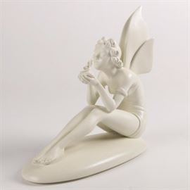 Handmade Resin Figurine of Fairy with Birdlings: A handmade resin figure of a fairy with birdlings. This piece, made of white resin, features a fairy girl with her legs extending in front of her. She is holding a best of birdlings with her face extended toward them. It bears a sticker to the underside reading “Handcrafted in China.”