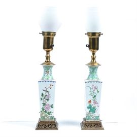 Pair of Asian Inspired Lamps: A pair of Asian inspired lamps. This pair of torchiere lamps are made of ceramic and brass and have a textured white glass shade. The ceramic column is decorated with Asian inspired art in shades of green pink and orange, and the square brass base has a center filagree of simple flowers.