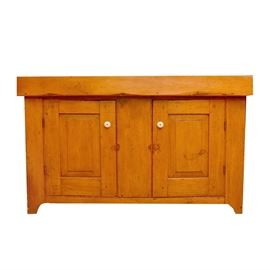 Antique Pine Dry Sink: An antique pine dry sink. The case features a rectangular top with raised edges above a pair of raised paneled doors. The doors are fitted with white knobs and open to shelf space. The back is finished with rough, horizontally set boards.