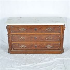 Victorian Era Marble Top Dresser: A Victorian era marble top dresser. This chest of drawers features three drawers, metal hardware including escutcheon and keyholes, fluted pilasters, and scrolled and acanthus leaf detailing. This item has no visible maker’s markings or labels.