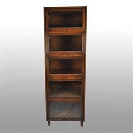 20th Century Oak Barrister Bookcase: A wooden five shelf oak barrister bookcase, circa the 20th century. A metal plate reads “5087” in the upper-right corner on the front. The five tiers feature functioning lifting glass windows that slide back for interior storage and a sliding shelf that can be pulled out for ease of access. The piece stands on round feet.