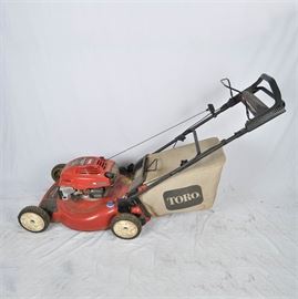 Toro Push Mower: A Toro brand push mower. The mower is red with a black handle and has a bag attached for clippings. On the top is reads “Guaranteed to start, 6.5 HP Engine.”