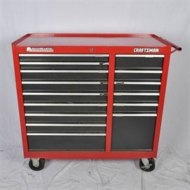 Craftsman Tool Chest With Tool Assortment: A craftsman tool chest with assorted tools. Inside are socket wrenches, various ball peen and sledge hammers, assorted pliers, ratchets, and much more. The red rectangular cabinets sit on black castor wheels.