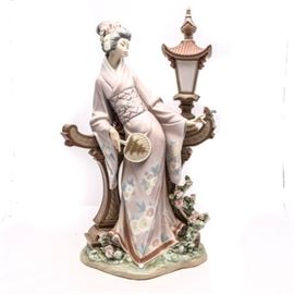 Lladró "Mariko" Figurine #1421: A Lladró porcelain figurine titled Mariko, #1421. The figurine depicts a Japanese woman clothed in a floral patterned kimono, she is holding a paddle fan decorated with a pagoda. Mariko is reclined against a brown stone wall with a small bird perched on the ledge. The delicate flowers in her hair match the flowers on the base. This model was originally sculpted by Salvador Debon in 1982 and was later retired in 1995.