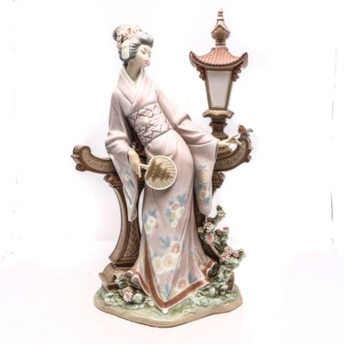 Lladró "Mariko" Figurine #1421: A Lladró porcelain figurine titled Mariko, #1421. The figurine depicts a Japanese woman clothed in a floral patterned kimono, she is holding a paddle fan decorated with a pagoda. Mariko is reclined against a brown stone wall with a small bird perched on the ledge. The delicate flowers in her hair match the flowers on the base. This model was originally sculpted by Salvador Debon in 1982 and was later retired in 1995.
