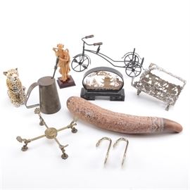 Assortment of Home Décor and Collectibles: An assortment of home décor and collectibles. This assortment approximately ten items of varying nature and use. Featured items include a smoked and carved Peruvian dried gourd with figural images; a metal tricycle sculpture, a metal trivet, a pair of brass hooks, one ceramic leopard, framed cork cutout scene, metal honey jar with a spoon, a carved wooden figurine, a metal basket and more.